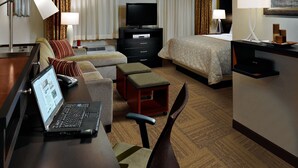 A hotel room with a bed, a desk with a laptop, a TV, a dresser, and a chair.