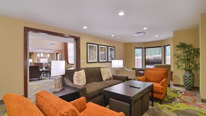A hotel lobby with a brown sofa, orange armchairs, a coffee table, and a dining area in the background.