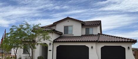 A two-story house with a tiled roof, two garage doors, and a landscaped front yard with rocks and small plants.
