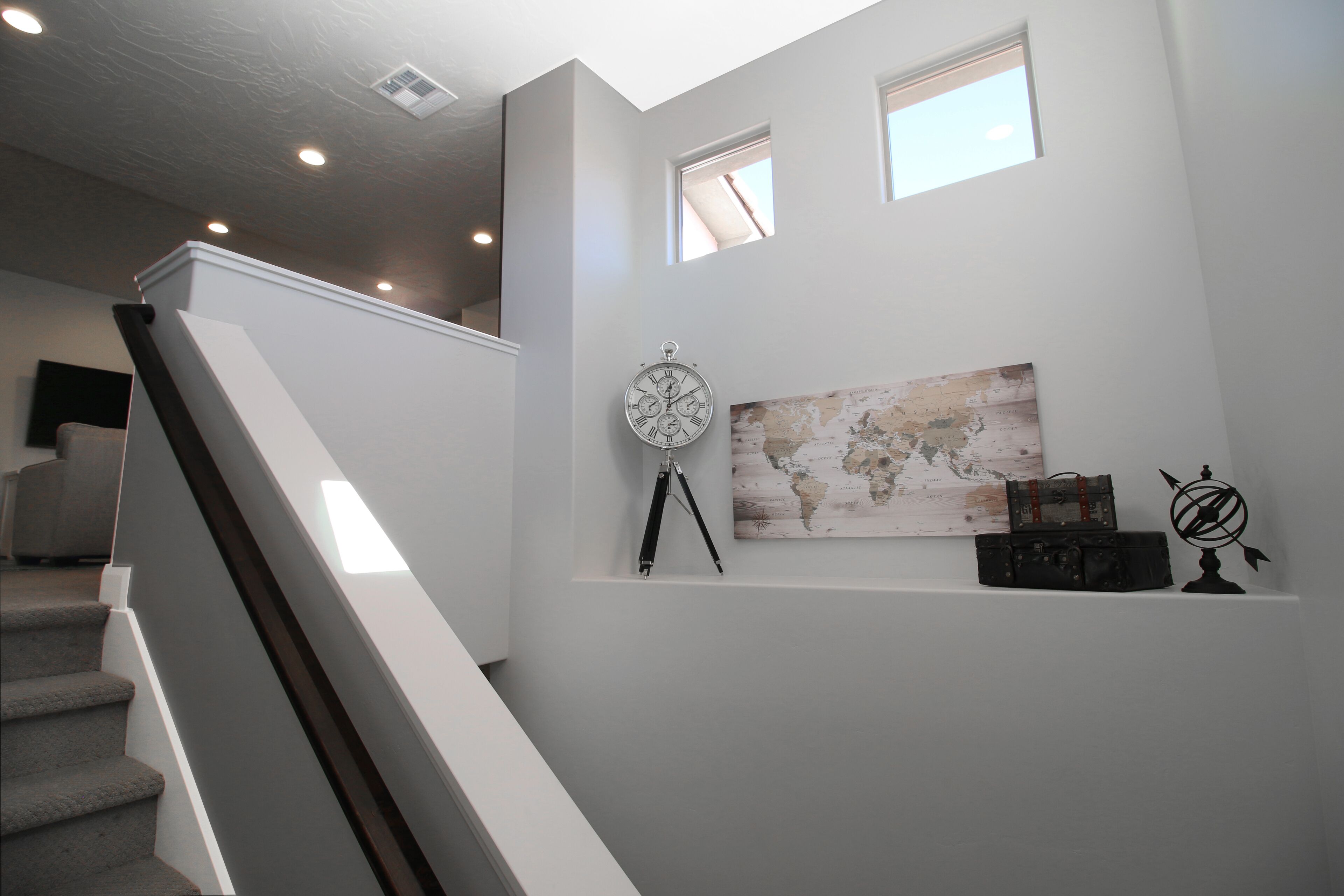A staircase leading to a landing with a world map, a compass, and a suitcase on a shelf.