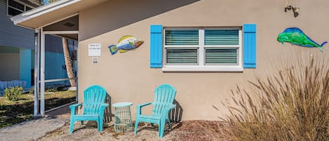 A building with a beige exterior, a window with blue shutters, and two turquoise chairs outside.