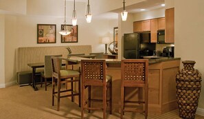 A compact kitchen with wooden cabinets, a dining area with a bench, and a large vase.