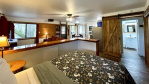 Een slaapkamer met een bed, een bureau, een stoel, een boekenkast en een badkamer met een wastafel en spiegel.