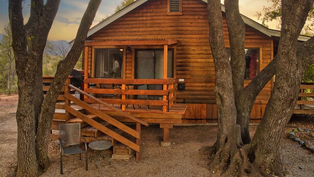 Een houten hut met een veranda, een trap en een kleine tafel met stoelen.
