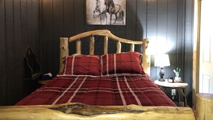Una cama de madera con cabecera, ropa de cama a cuadros rojos y un cuadro de caballos en la pared.