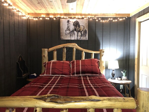 Una cama de madera con cabecera, ropa de cama a cuadros rojos y un cuadro de caballos en la pared.