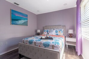 A bedroom with a bed, nightstands, a painting, and a window with blinds.