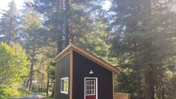 A small cabin with a red door, a bench outside, and a gravel path leading to it.