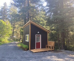 A small cabin with a red door, a bench outside, and a gravel path leading to it. - Cute & Cozy Tiny House in the Woods (Seward)
