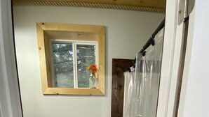 A small bathroom with a toilet, a window with a flower, and a shower curtain.