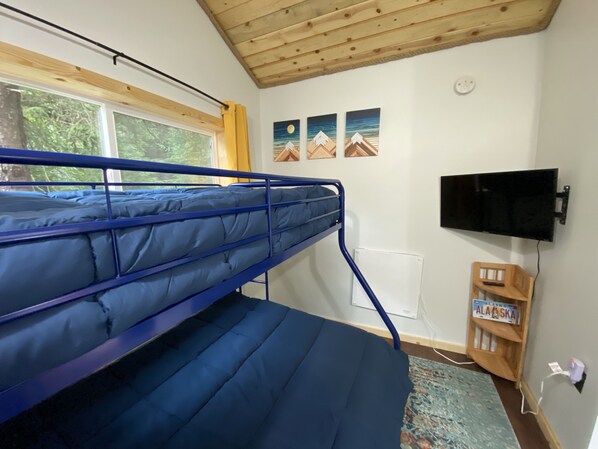 A bunk bed room with a window, a mounted TV, and a wooden shelf with a license plate. - Cute & Cozy Tiny House in the Woods (Seward)
