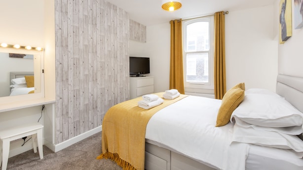 A hotel room with a bed, a desk with a mirror, a television, and a window with curtains.