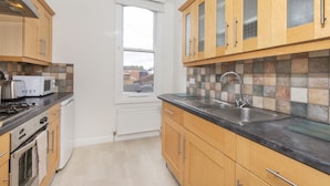 A modern kitchen with wooden cabinets, a black countertop, stainless steel appliances, and a window with a view.