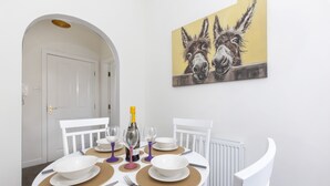 A dining area with a round table set for four, white chairs, and a painting of donkeys on the wall.