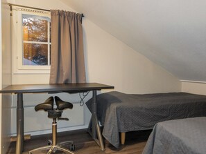 Een kamer met een bureau, twee bedden, een raam met gordijnen en een stoel met een camera.