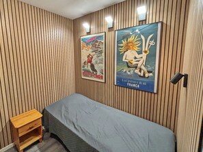Una stanza con pareti rivestite in legno, un letto con materasso grigio e due poster appesi al muro.