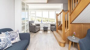 A modern living room with a staircase, large windows, and a view of the outdoors.