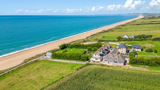 A coastal property with a beach view, multiple houses, and a large field.