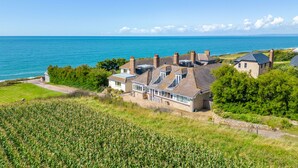 A coastal house with a large bay window, a stone chimney, and a view of the sea.