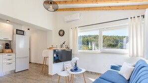 A modern living room with a blue sofa, a small table with a vase, and a kitchen area with a microwave and refrigerator. - Villa Likva - Two Bedroom Villa with Private Pool and Hot Tub (Sutivan)