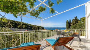 A covered outdoor seating area with wooden loungers and a table, overlooking a scenic view of the sea and hills. - Villa Likva - Two Bedroom Villa with Private Pool and Hot Tub (Sutivan)