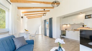A modern living room with a blue sofa, a white coffee table, and a vase with flowers. There is a kitchen with white cabinets and a microwave. - Villa Likva - Two Bedroom Villa with Private Pool and Hot Tub (Sutivan)