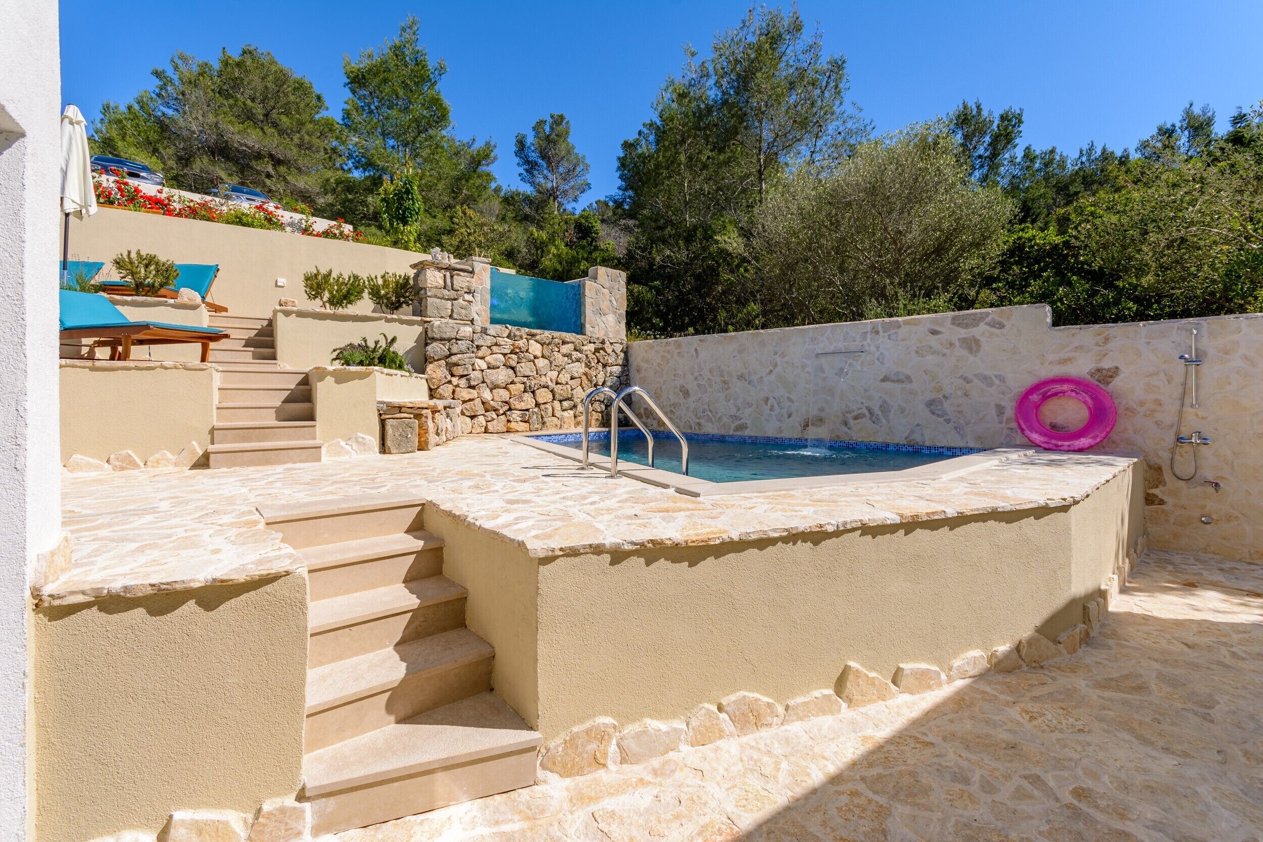 A swimming pool with a stone wall, steps leading to a lounge area, and a pink floatation device.