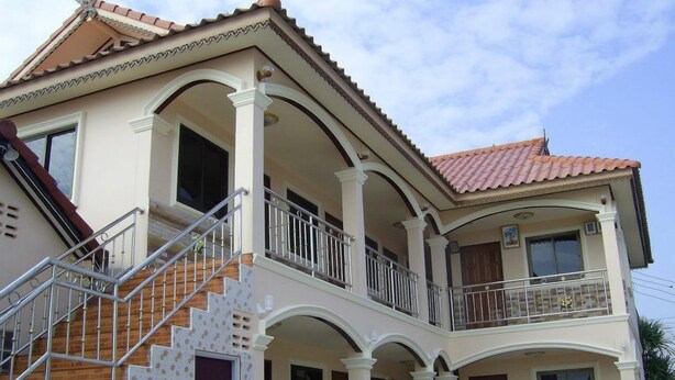 Uma casa de dois andares com varanda, escadaria e telhado de telhas.