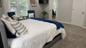 A bedroom with a large bed, a TV mounted on the wall, and a door leading to another room. - Great Comfortable Private Studio (Barnstable)