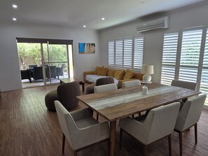 A modern dining area with a wooden table, cushioned chairs, and a sofa with cushions. - Breath of Fresh Eyre | Walk to Town & Coastal Comfort (Dunsborough)