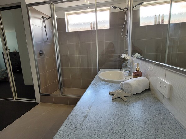 Un baño moderno con ducha envuelta en vidrio, lavamanos con espejo y artículos de tocador sobre la encimera.