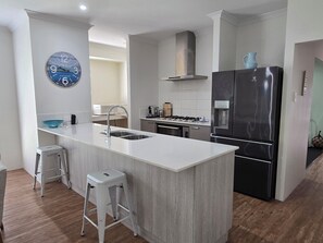 A modern kitchen with a central island, stainless steel appliances, and a clock on the wall. - Breath of Fresh Eyre | Walk to Town & Coastal Comfort (Dunsborough)