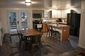 A modern kitchen with a dining area, featuring a wooden table and chairs, a built-in oven, a microwave, and a refrigerator. - Short walk to the lake! (Huntingdon)
