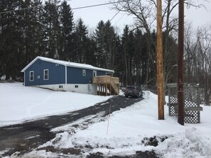 A blue house with a wooden deck, surrounded by snow-covered ground and trees. - Short walk to the lake! (Huntingdon)