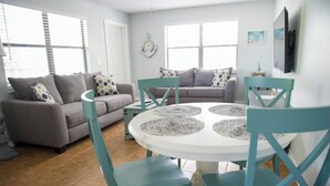 Un salon avec un canapé gris, des fauteuils turquoise et une table ronde blanche agrémentée de sets de table.