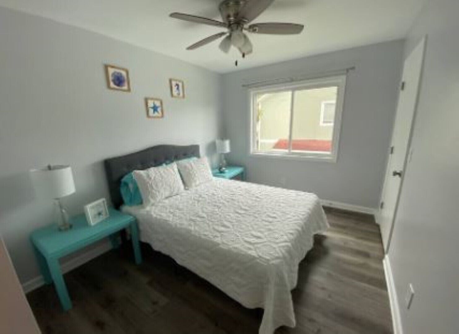 Ein Schlafzimmer mit Bett, Nachttisch, Lampe, Deckenventilator und Fenster.