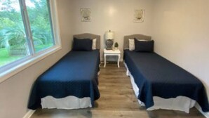 A room with two single beds, a small table with a lamp, and a ceiling fan.