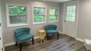 A room with three blue chairs, a small yellow table, and a white door.
