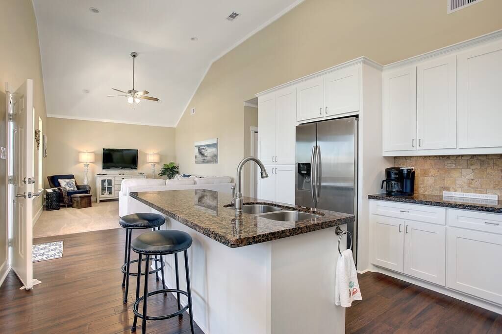 A modern kitchen with white cabinets, a granite countertop, a stainless steel refrigerator, and a bar stool.