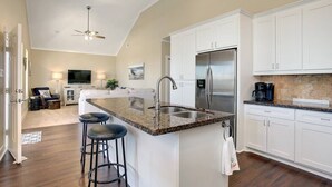 A modern kitchen with white cabinets, a granite countertop, a stainless steel refrigerator, and a bar stool. - 3 BR Beach view -For the Good Times Beach House (Galveston)