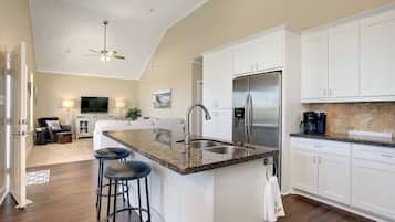 A modern kitchen with white cabinets, a granite countertop, a stainless steel refrigerator, and a bar stool.