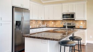 A kitchen with white cabinets, stainless steel appliances, a granite countertop, and a 'Beach' backsplash. - 3 BR Beach view -For the Good Times Beach House (Galveston)