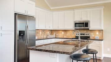 A kitchen with white cabinets, stainless steel appliances, a granite countertop, and a 'Beach' backsplash.