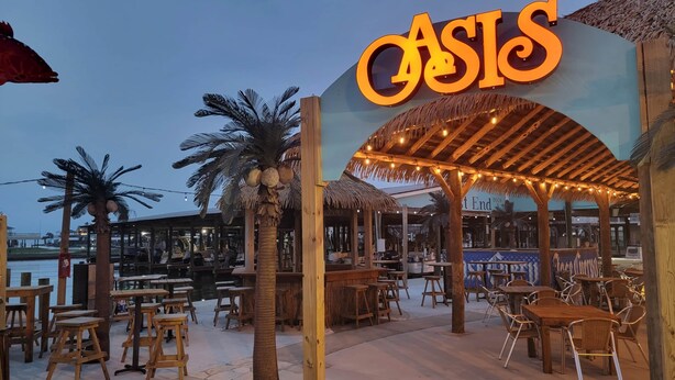 A beachside restaurant named 'Oasis' with outdoor seating and a thatched roof structure. - 3 BR Beach view -For the Good Times Beach House (Galveston)