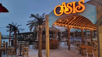 A beachside restaurant named 'Oasis' with outdoor seating and a thatched roof structure.