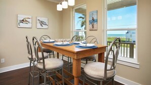 A dining area with a wooden table set for four, metal chairs, and artwork on the walls. - 3 BR Beach view -For the Good Times Beach House (Galveston)