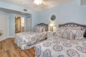 A bedroom with two beds, a ceiling fan, a bedside lamp, and a mirror. - Catch n` Relax - Ocean Walk (Daytona Beach)