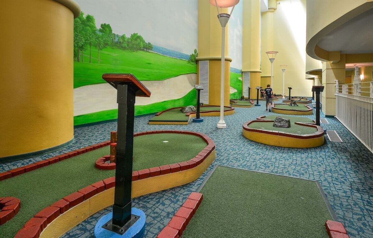 A miniature golf course with a green landscape mural in the background, a series of holes with flags, and a patterned floor.