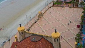 A beachside view with a pier extending into the ocean, a paved walkway, and a building with a red-tiled roof. - Lattitude Adjustment - Ocean Walk (Daytona Beach)