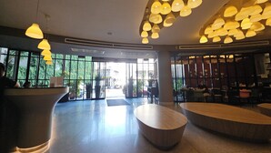 Un hall d’entrée spacieux avec un comptoir de réception, plusieurs espaces aménagés pour s’asseoir et de grandes fenêtres offrant une vue sur l’extérieur.